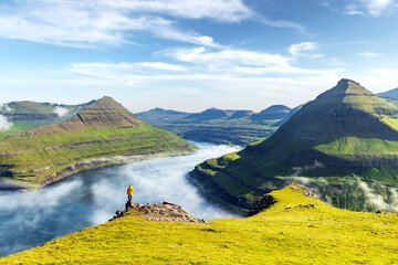 Wall Mural - Lonely tourist in yellow jacket looking over majestic fjords of Funningur, Eysturoy island, Faroe Islands. Landscape photography