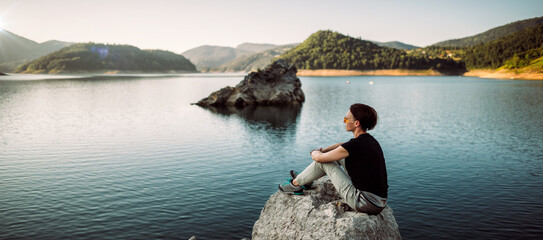 a young woman sitting on a rock by the lake