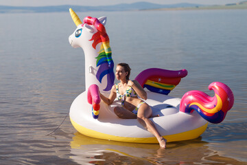 Girl swimming on white, trendy, blown up beach unicorn in summer in a pond