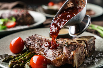 Wall Mural - Delicious grilled beef steak with spices on plate with tomatoes and berry sauce over dark background. Concept of bbq food, close up