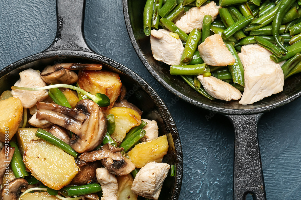 Frying pans with tasty vegetables and chicken on color background, closeup