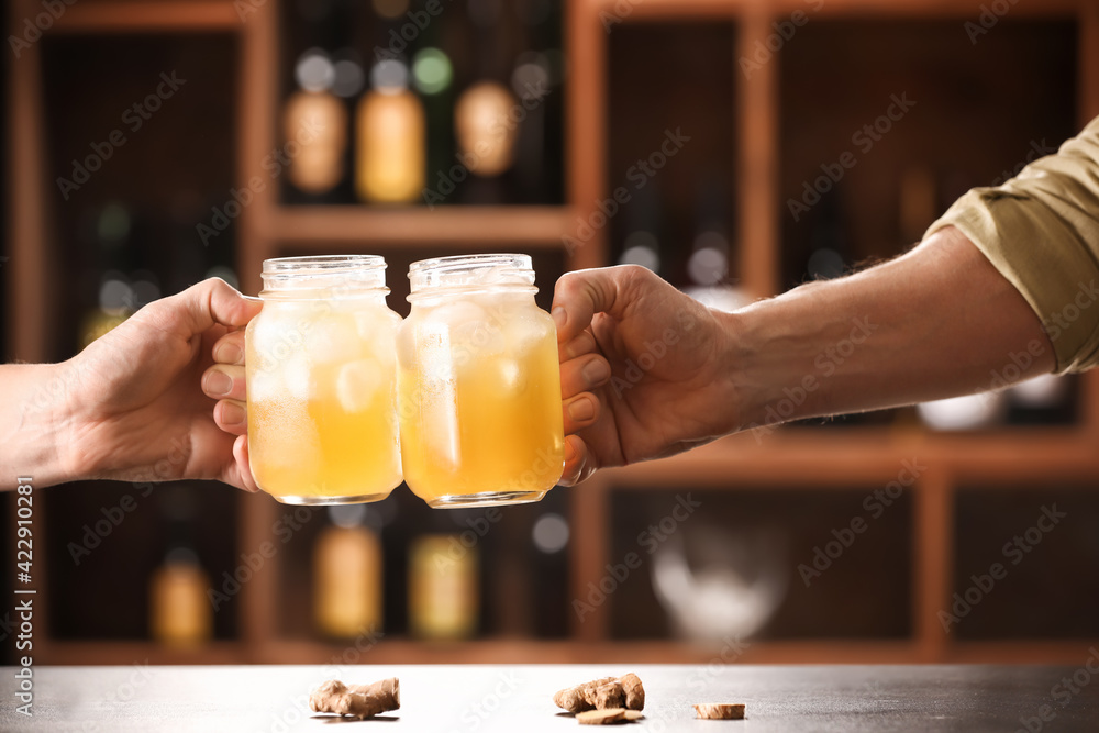 Men clinking mason jars of fresh ginger beer on table in bar