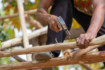 Close-up of a man hammering nails on a eucalyptus wood roof frame. House design using miniature eucalyptus