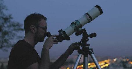 Wall Mural - astronomer with a telescope watching at the stars and moon with blurred city lights in the backgroun