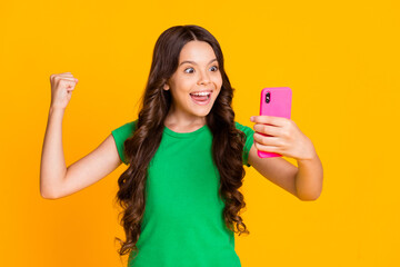 Poster - Photo of happy cheerful smiling funky crazy girl raise fist in victory use smartphone isolated on yellow color background