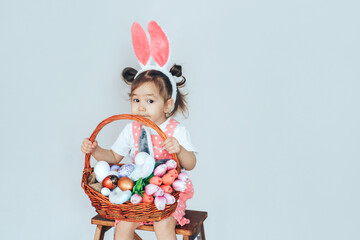 Canvas Print - Little girl dressed as rabbit holding large basket filled with eggs and tulips against white background