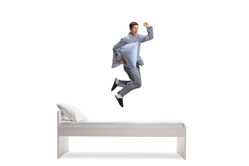 Wall Mural - Full length shot of a man in pajamas holding a pillow and jumping on a bed