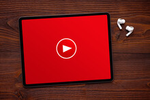 Play button on the screen of tablet and wireless earphones on dark wooden surface