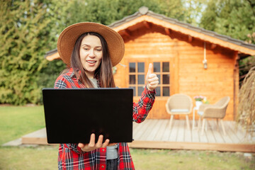 young gardener shows her wooden garden shed on a laptop. woman with a straw hat is standing in the g