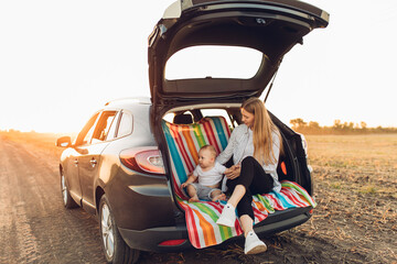 Wall Mural - Happy family, a young mother with a child sitting in the trunk of a car, traveling