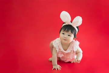 Baby in Easter bunny hairband. Asian happy baby smiling and crawling on red background. Cute 6 months baby crawling with copy space as Easter concept, baby or kid department in hospital.