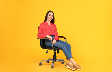 Wall Mural - Young woman sitting in comfortable office chair on yellow background