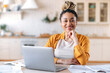 © Kateryna - Satisfied good looking young African American stylish woman, freelancer, student or real estate agent, sitting at her desk at home office, looking at the camera and smiling pleasantly