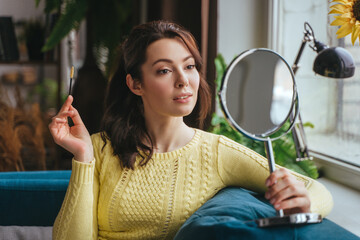 Young pretty woman does makeup at home while looking in the mirror