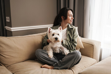 Happy white woman resting with her dog on sofa at home