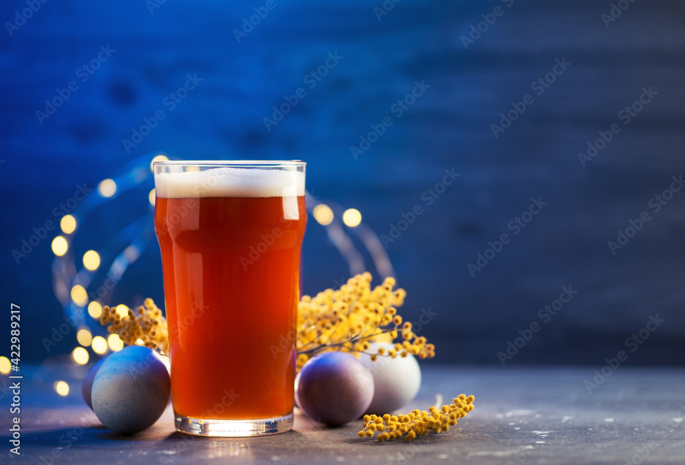 Limited edition craft beer pint glass on blue background, painted Easter eggs. The concept of celebrating Easter, copy space - obrazy, fototapety, plakaty 