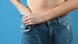 © Tatsiana - Woman shows that she has lost weight and her old jeans got too large, blue background with copy space