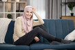© sofiko14 - Portrait of cheerful Muslim woman in hijab posing on sofa at home, relaxing in living room, enjoying weekend or leisure time