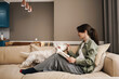 Happy white woman reading book while resting with her dog on sofa