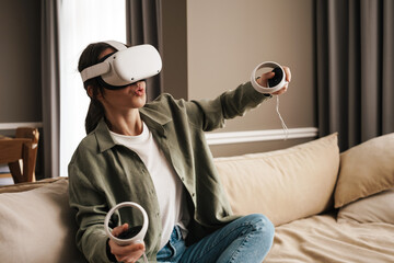 Wall Mural - Excite white woman playing online game with vr glasses and controllers