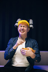 Young male sits on a sofa and eats snacks while watching a movie. Handsome man with beer helmet on the head watching TV and eating potato chips on the couch at home