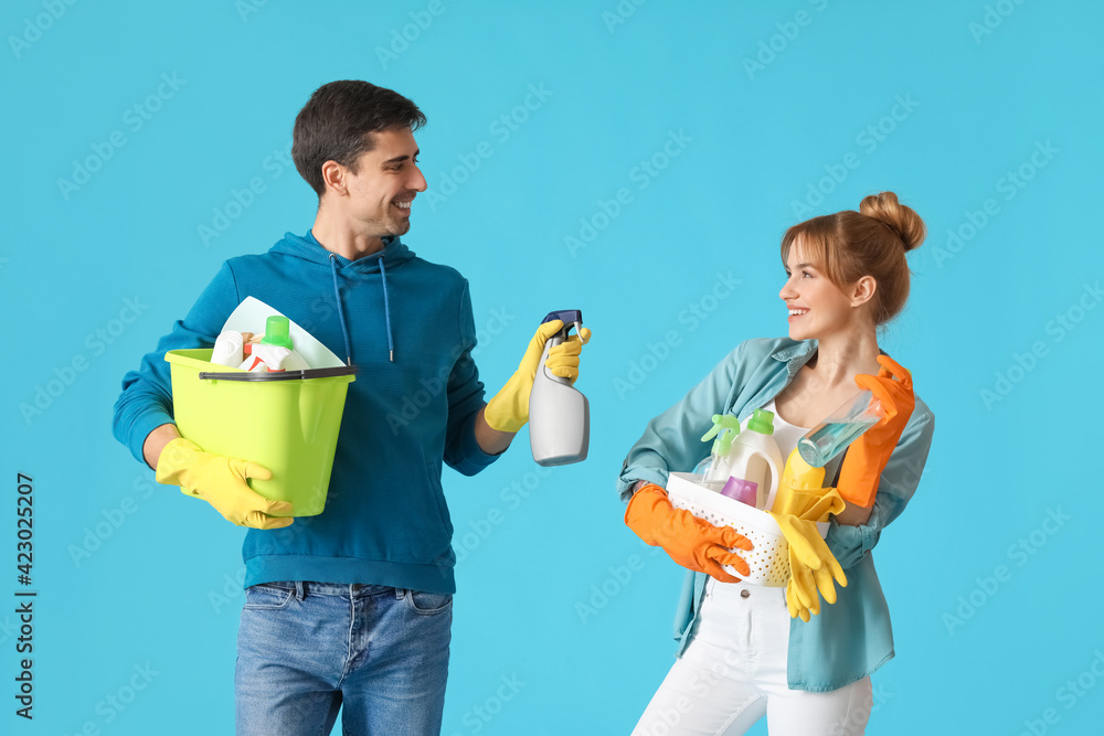 Young couple with cleaning supplies on color background