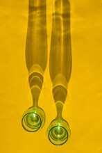 Two Glasses Of Green Glass On A Yellow Background. Glass Shade From Sunlight. View From Above. Vertical Photo. Long Shadow.
