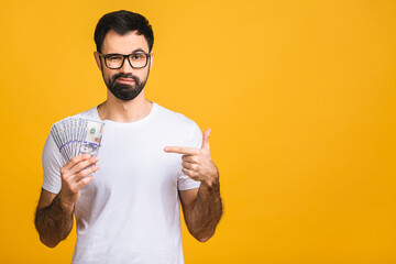 Wall Mural - Happy winner! Young rich man in casual holding money dollar bills with surprise isolated over yellow background.