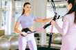 © Iryna - Two happy smiling positive girls are talking before TRX training in the gym on modern interior background. They are wearing pink sportswear.