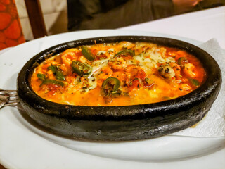 Wall Mural - Baked fish with vegetables in a creamy sauce lies in a black frying pan