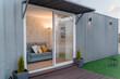 © Jake Jakab/ADDICTIVE STOCK - Contemporary gray container house with comfy sofa behind glass door located on grassy yard