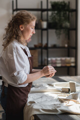 A young potter woman making pot in her own working place. Standing in spacious studio creating the shape of the future product with her hands.