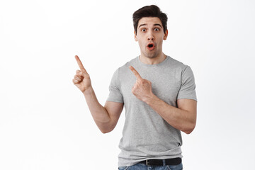 Portrait of fascinated and amazed handsome man pointing left, showing copy space for logo or banner, standing over white background