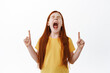 Little red haired girl screaming and pointing fingers up. Ginger kid with freckles shouting and showing something aside on copy space, white background
