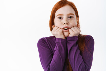 Wall Mural - Fascinated little redhead girl look with interest and amazement, stare at something breathtaking and impressive, standing amazed against white background