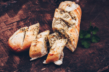 Tasty bread with garlic, butter and herbs on old wooden table