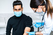 © Тарас Нагирняк - A handsome Indian man in a protective mask during a vaccination against Covid 19, a female doctor injects him in the arm