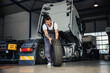 © Dusan Petkovic - Smiling hardworking mechanic rolling tire in order to change it on truck. He is in garage of import and export firm.