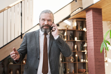 Wall Mural - Confident mature businessman having a conversation on mobile phone while going to the meeting in the restaurant