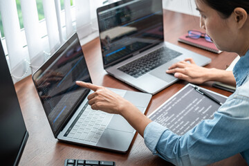 Wall Mural - asian programmer woman pointing and looking on multiple laptop screen to writing code and database