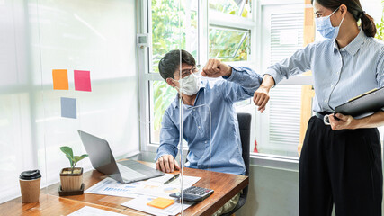 Wall Mural - Two business colleagues greet each other by bumping elbows when meeting in office while wearing face mask