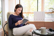 © Freedomz - Young asian woman sitting to relaxing on comfortable armchair and reading book while rest on holiday