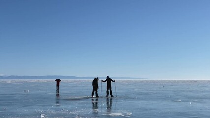 Wall Mural - The guys are testing the ice for strength. Travel on frozen Lake Baikal. Beautiful winter landscape with blue transparent ice with deep cracks and islands of snow.