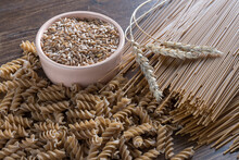 Spelt pasta with seeds and ears on wooden table.