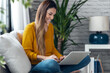 © nenetus - Pretty young woman working with her laptop while sitting on couch at home.