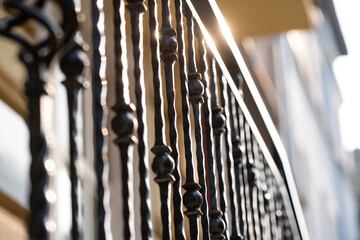 Beautiful iron black decorative carved old railing by the stairs, made by a blacksmith illuminated by the sun on a day close up 