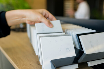 Close up of young woman interior designer choosing elements of materials for the kitchen in a new home holding the stone in hands. House renovation concept. Selective focus on foreground