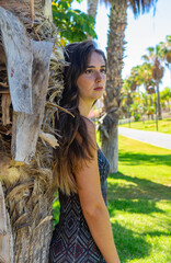 Wall Mural - Portrait of young woman leaning on a palm tree. She wears a short dress. It is located in Las Americas, Tenerife