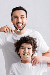 Wall Mural - Smiling muslim man brushing teeth near son in bathroom