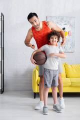 Wall Mural - Cheerful muslim son and father pointing at basketball at home